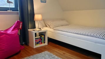 A bedroom with a bed, a nightstand with a lamp, a bookshelf, and a window with a bird decoration.