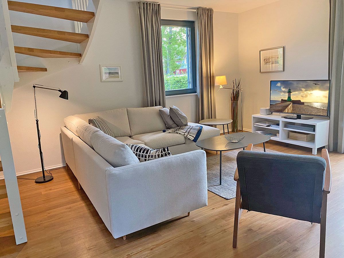 A modern living room with a sofa, coffee table, and a chair. There is a TV on a stand, a lamp, and a window with curtains.