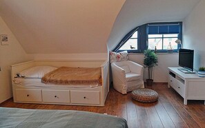 Ein Schlafzimmer mit einem Bett, einem weißen Sofa, einem TV-Schrank und einem Fenster mit Jalousien.