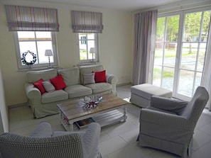 A living room with a sofa, armchairs, a coffee table, and a view through large windows. - Vacation home with a fireplace and sauna, about 450 meters from the sandy beach, washing machine, dryer (Glowe)