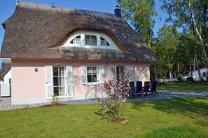 A house with a thatched roof, white shutters, and a small garden with a flowering plant. - Vacation home with a fireplace and sauna, about 450 meters from the sandy beach, washing machine, dryer (Glowe)