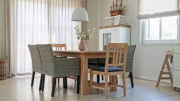 Uma sala de jantar com mesa de madeira, cadeiras de vime, um vaso com flores e um modelo de navio em uma estante.