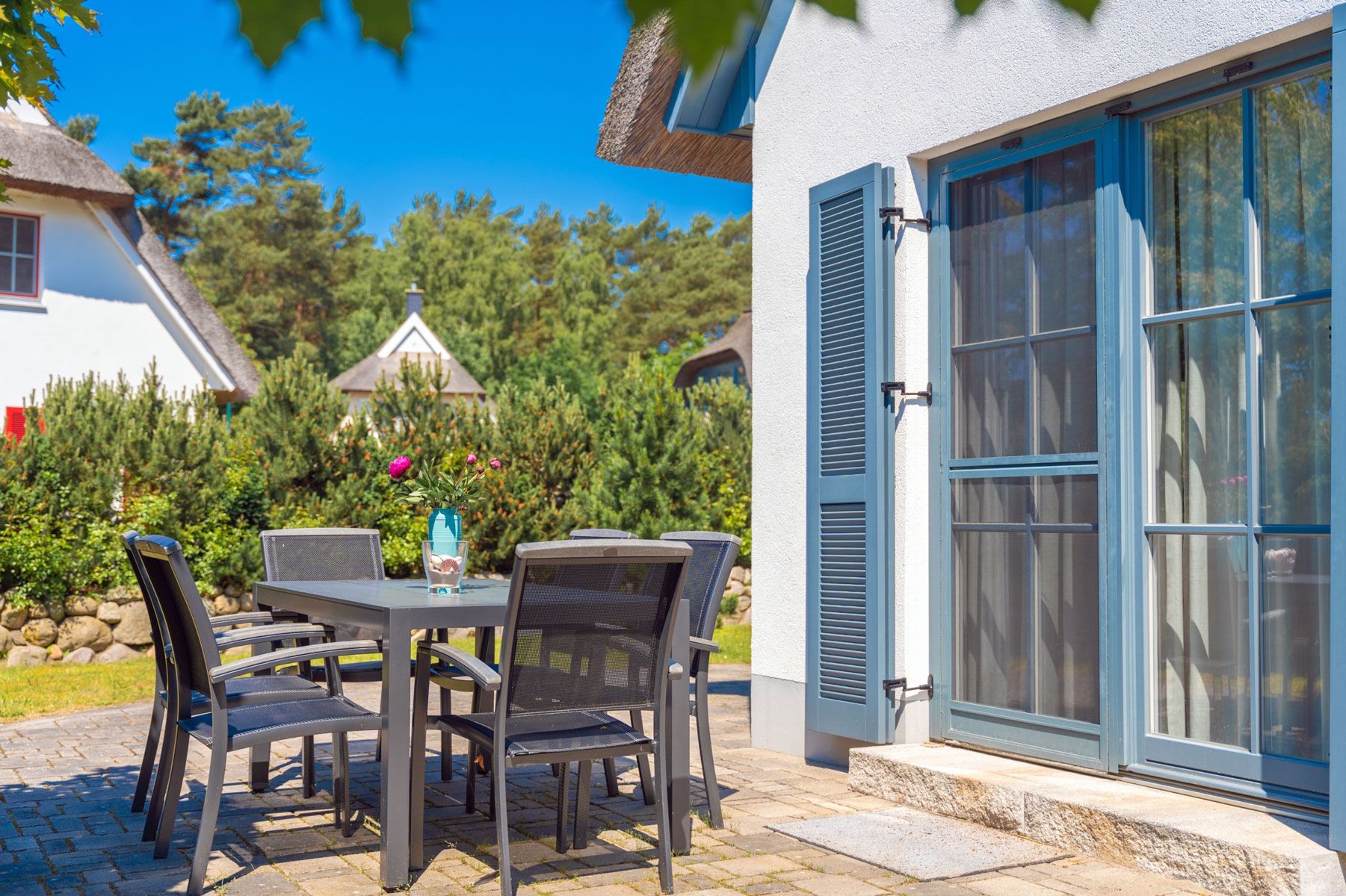An outdoor patio with a table and chairs, a blue door, and a white building in the background.
