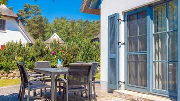 An outdoor patio with a table and chairs, a blue door, and a white building in the background.