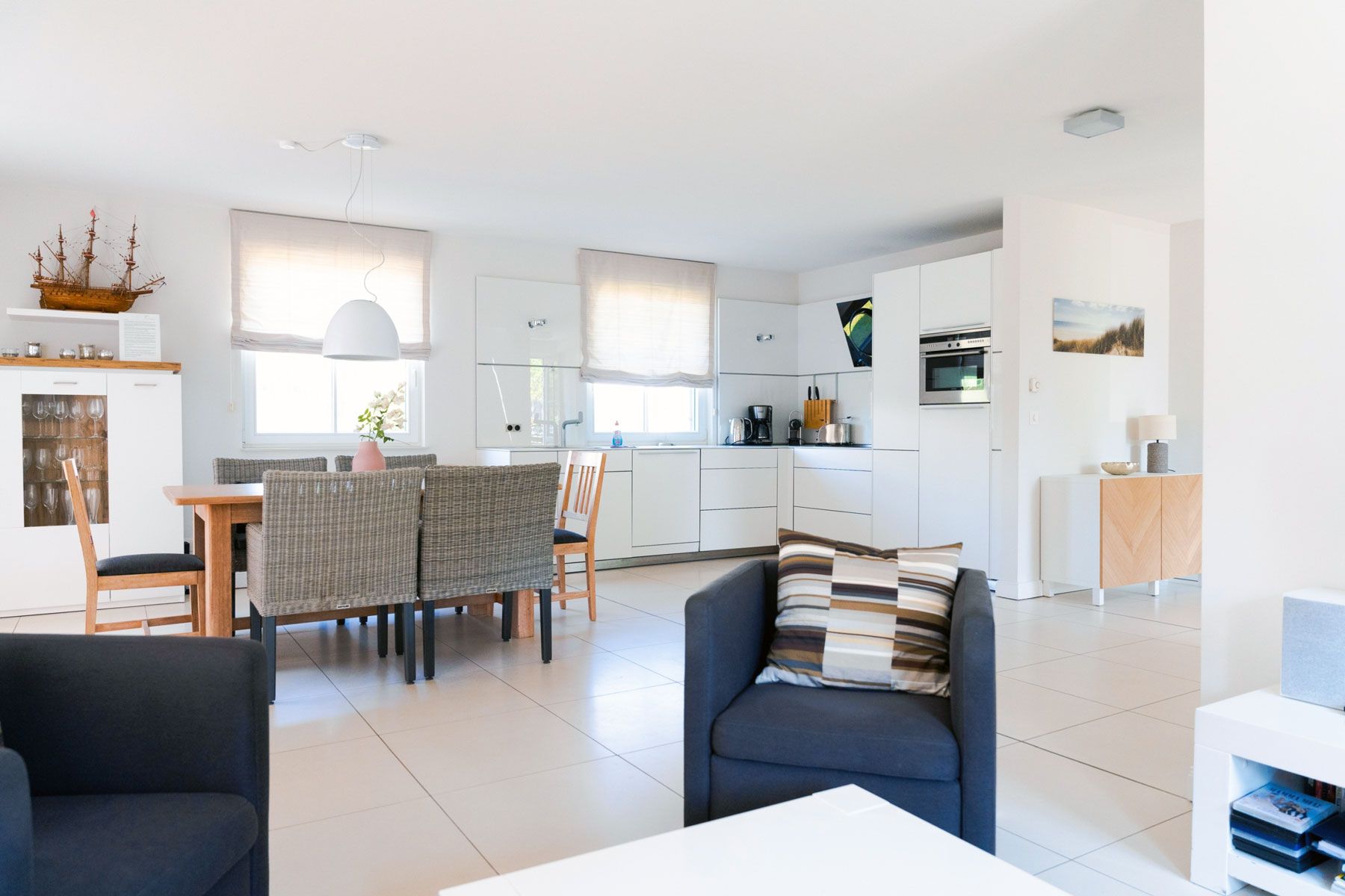 A modern kitchen with white cabinets, a dining area with wicker chairs, and a living space with a sofa and a coffee table.