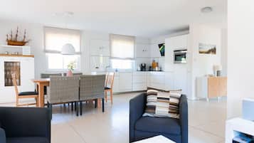 A modern kitchen with white cabinets, a dining area with wicker chairs, and a living space with a sofa and a coffee table.
