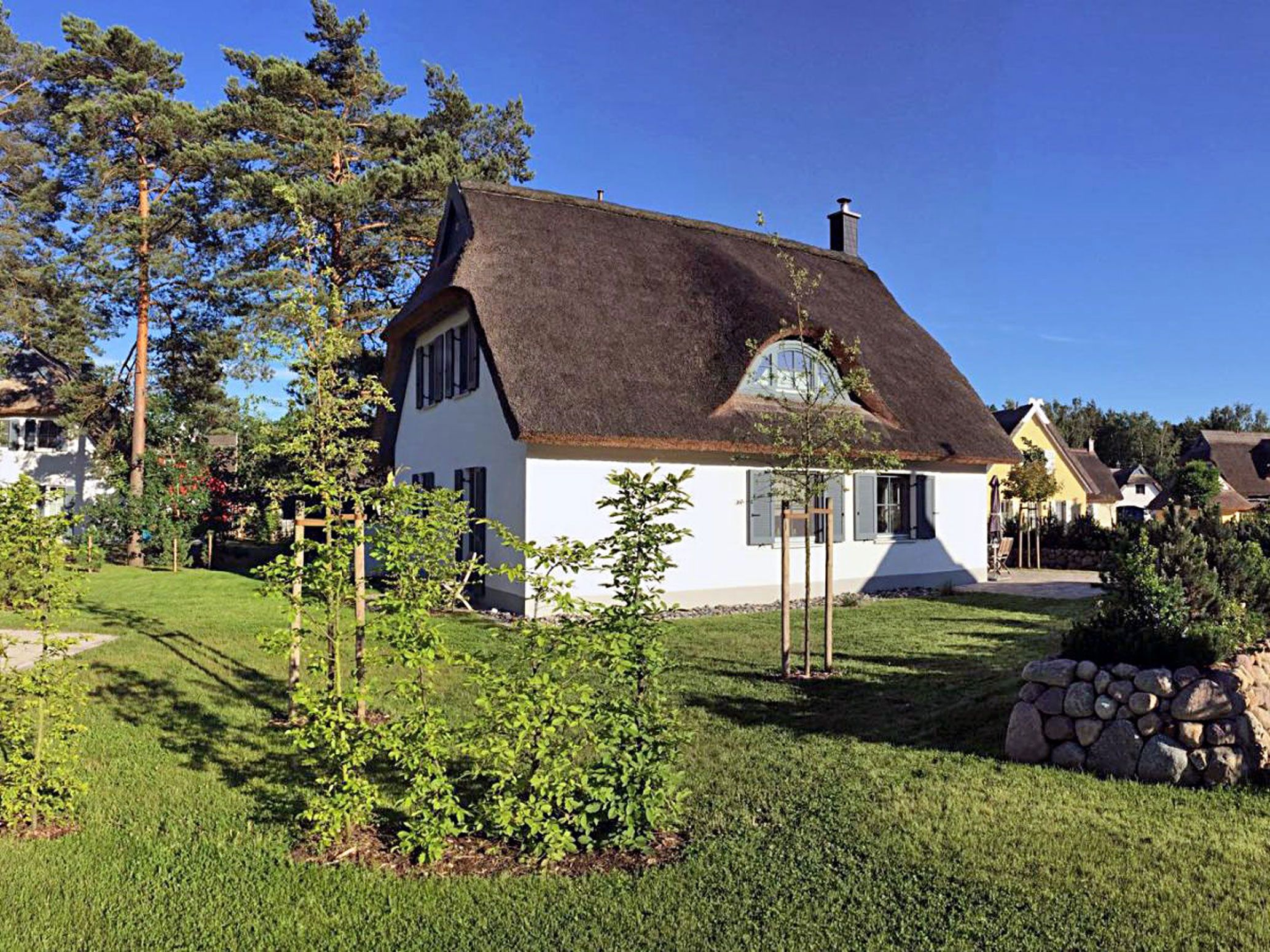 Een huis met rieten dak, omgeven door een verzorgd gazon en bomen.