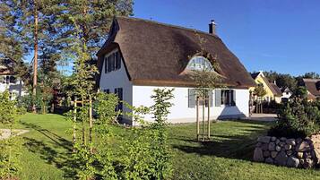 Een huis met rieten dak, omgeven door een verzorgd gazon en bomen.