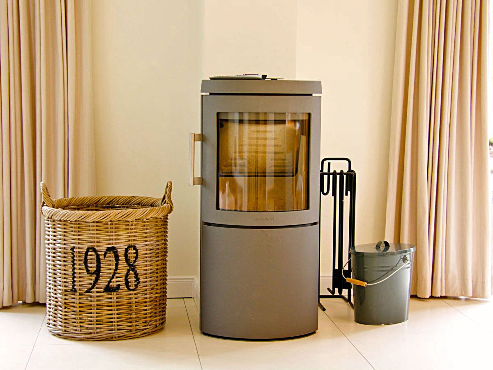 A room with a modern heating unit, a wicker basket with the number 1928, and a metal bucket.