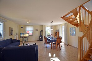 A spacious living area with a sofa, dining table, and a wooden staircase. - Vacation home with a fireplace, about 400 meters from the sandy beach, with a washing machine and Wi-Fi (Glowe)