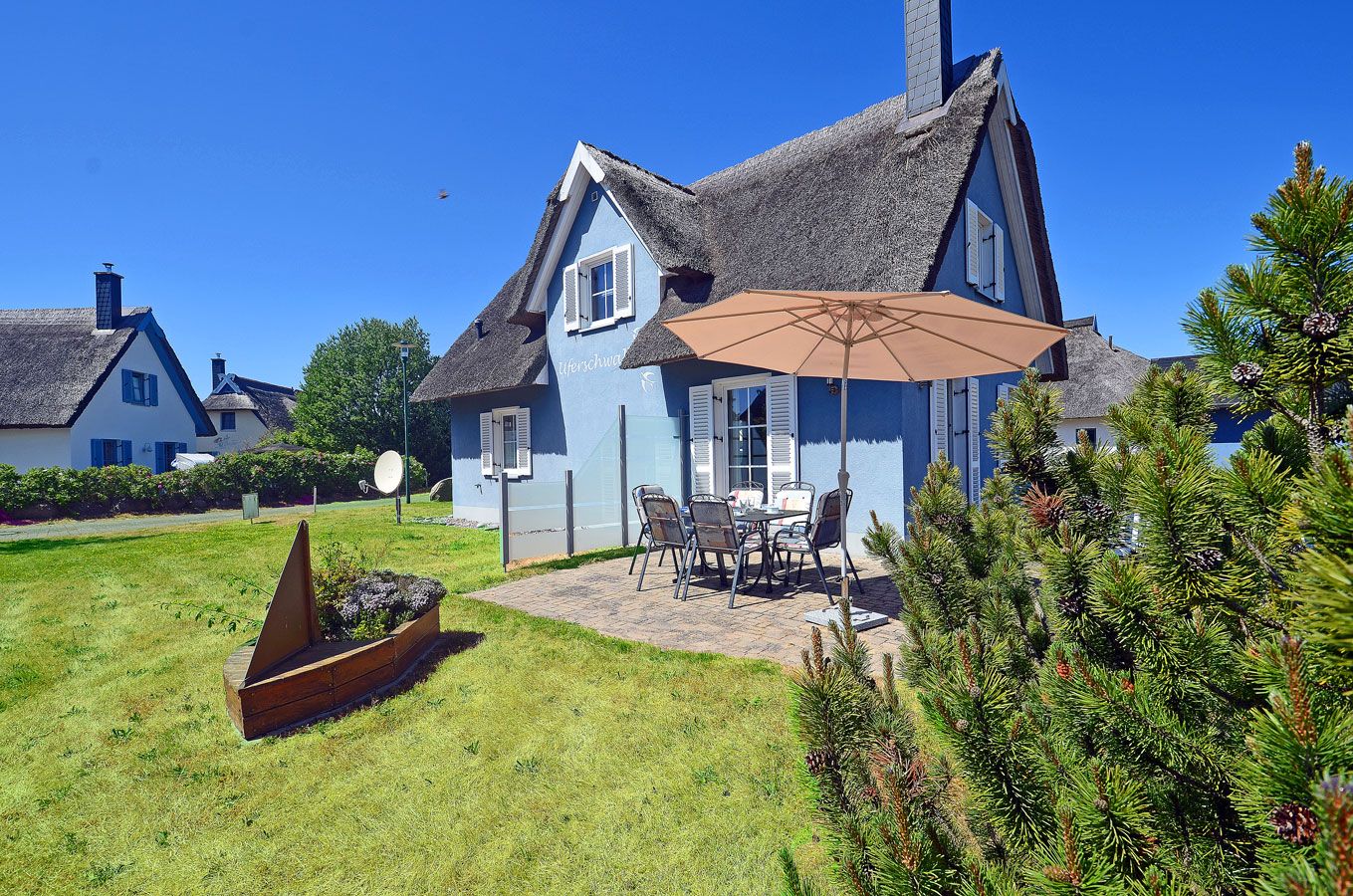A traditional house with a thatched roof, a patio with outdoor furniture, and a well-maintained lawn.