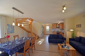 A dining area with a wooden staircase, a kitchen in the background, and a living room with a sofa. - Vacation home with a fireplace, about 400 meters from the sandy beach, with a washing machine and Wi-Fi (Glowe)