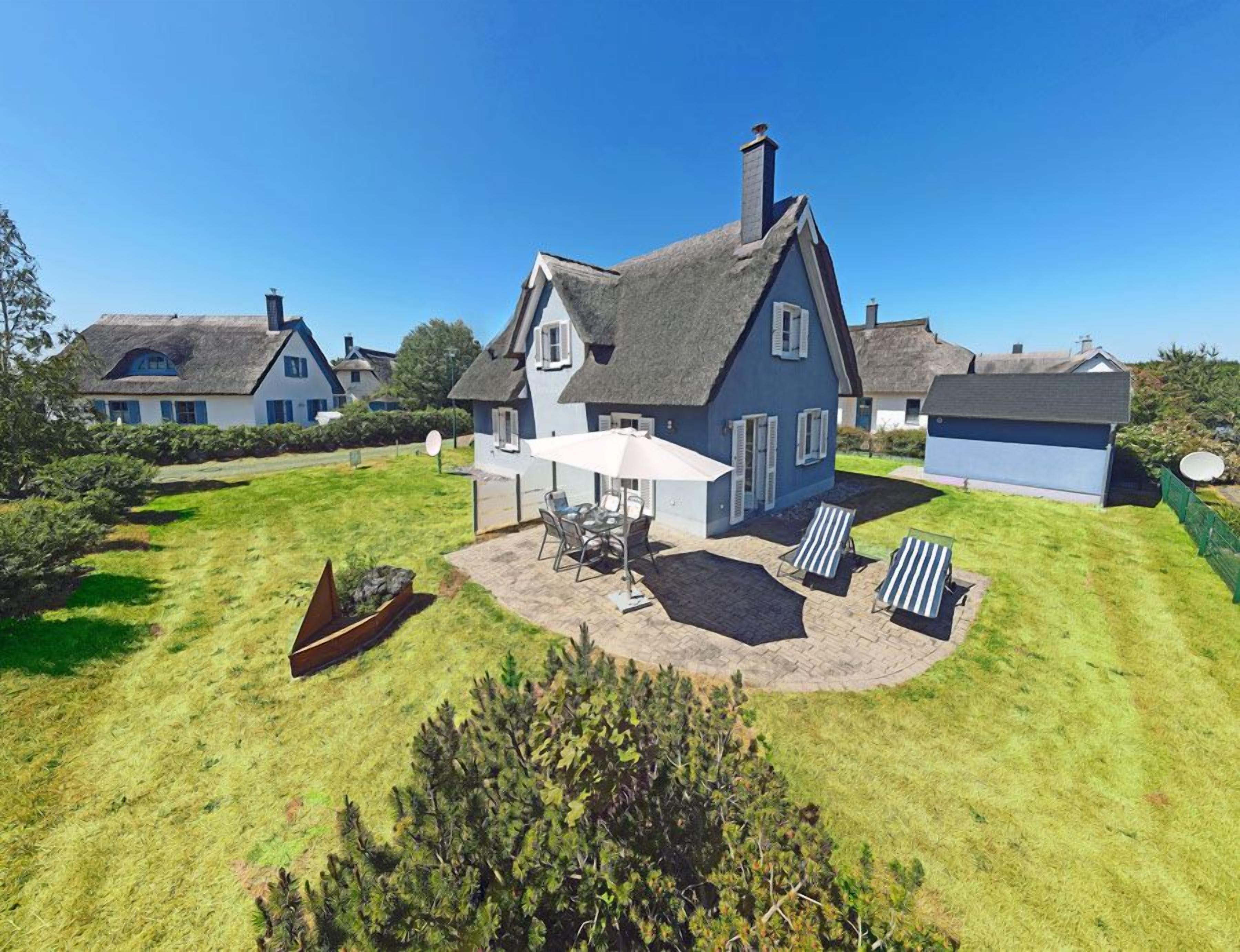 Une grande maison avec un toit de chaume, une terrasse avec des meubles d’extérieur et un bateau dans la cour.