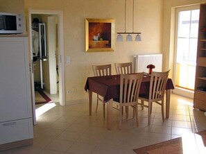 Un coin repas avec une table et des chaises, un réfrigérateur, un tableau accroché au mur et une fenêtre avec des stores.