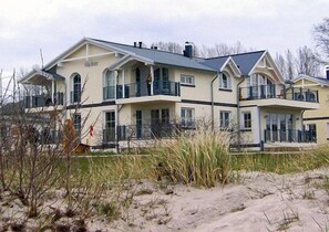 A large, two-story building with multiple balconies, located near a sandy area with vegetation. - Right on the sandy Baltic Sea beach with a view of the sea!, Wi-Fi, washing machine, accommodates up to 3 people (Glowe)