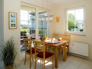 A dining area with a table set for two, wooden chairs, a potted plant, and a view of the outside. - Right on the sandy Baltic Sea beach with a view of the sea!, Wi-Fi, washing machine, accommodates up to 3 people (Glowe)