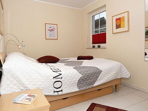 A bedroom with a bed, a bedside table with a book, a window with blinds, and a framed picture on the wall. - Right on the sandy Baltic Sea beach with a view of the sea!, Wi-Fi, washing machine, accommodates up to 3 people (Glowe)