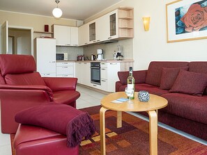 A living room with a red sofa, a red armchair, and a small round table with a bottle and glass. - Right on the sandy Baltic Sea beach with a view of the sea!, Wi-Fi, washing machine, accommodates up to 3 people (Glowe)