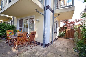 Un patio con una mesa y sillas, una cerca de madera y un edificio con balcón.