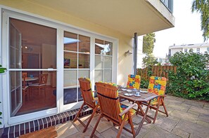 Un patio con una mesa y sillas, un cerramiento de vidrio corredero y vista a la calle.