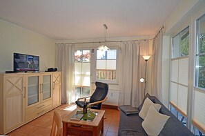 A living room with a television, a sofa, a chair, a table with a bottle and glasses, and a lamp. - Just 50 meters from the sandy Baltic Sea beach, Wi-Fi, accommodates up to 4 people, with a covered patio (Glowe)