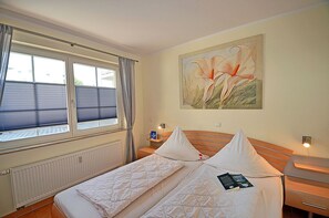 Una habitación de hotel con cama, mesita de noche, ventana con cortinas y un cuadro en la pared.