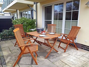 An outdoor patio with a wooden table and four chairs, a bowl of fruit, and a wine glass. - Just 50 meters from the sandy Baltic Sea beach, Wi-Fi, accommodates up to 4 people, with a covered patio (Glowe)