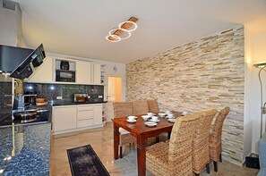A modern kitchen with white cabinets, a black countertop, and a dining area with wicker chairs and a wooden table set for four. - Just 50 meters from the sandy Baltic Sea beach, Wi-Fi, washer/dryer, sleeps up to 4 people, with a terrace (Glowe)