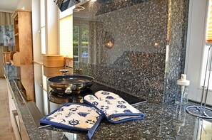 A kitchen with a granite countertop, a stove, and a pair of oven mitts. - Just 50 meters from the sandy Baltic Sea beach, Wi-Fi, washer/dryer, sleeps up to 4 people, with a terrace (Glowe)