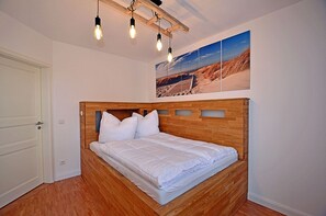 A bedroom with a wooden bed, white bedding, and a ceiling light fixture. - Just 50 meters from the sandy Baltic Sea beach, Wi-Fi, washer/dryer, sleeps up to 4 people, with a terrace (Glowe)
