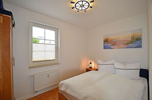 Een slaapkamer met een bed, een raam, een radiator, een aan de muur hangend schilderij en een plafondlamp.