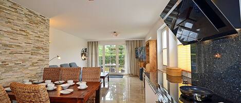 A modern kitchen with a black countertop, a dining area with wicker chairs, and a stone wall.