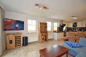 A living room with a television, a wooden cabinet, a sofa, and a kitchen area. - Just 50 meters from the sandy Baltic Sea beach, Wi-Fi, washer/dryer, sleeps up to 4 people, with a terrace (Glowe)