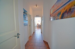 A hallway with a tiled floor, a door on the left, and a painting on the right. - Just 35 meters from the sandy Baltic Sea beach, Wi-Fi, 2 bedrooms, sleeps up to 5 people, with a balcony (Glowe)