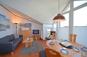 A modern living room with a sofa, TV, and dining area with a table set for two. - Just 35 meters from the sandy Baltic Sea beach, Wi-Fi, 2 bedrooms, sleeps up to 5 people, with a balcony (Glowe)
