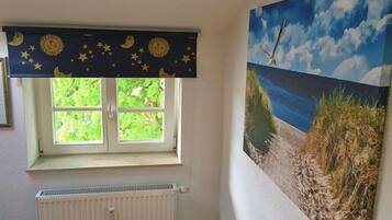 A room with a window, a radiator, and a beach mural on the wall.