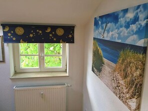 Une pièce avec une fenêtre, un radiateur et une fresque murale représentant une plage.
