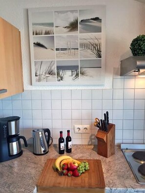 Une cuisine avec une planche à découper en bois, des bananes, des raisins et des fraises. On y trouve une machine à café, un grille-pain et un bloc à couteaux.