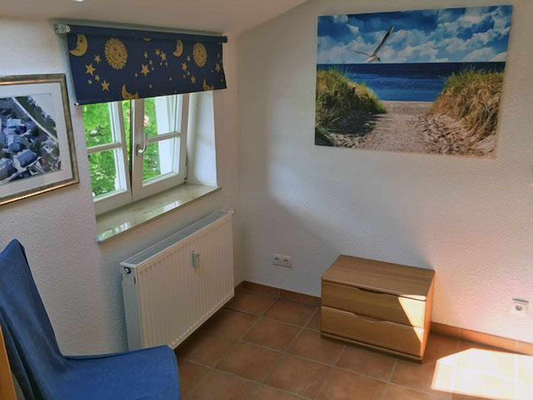 A room with a window, a radiator, a chair, a small table, and a painting on the wall.