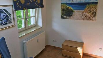 A room with a window, a radiator, a chair, a small table, and a painting on the wall.
