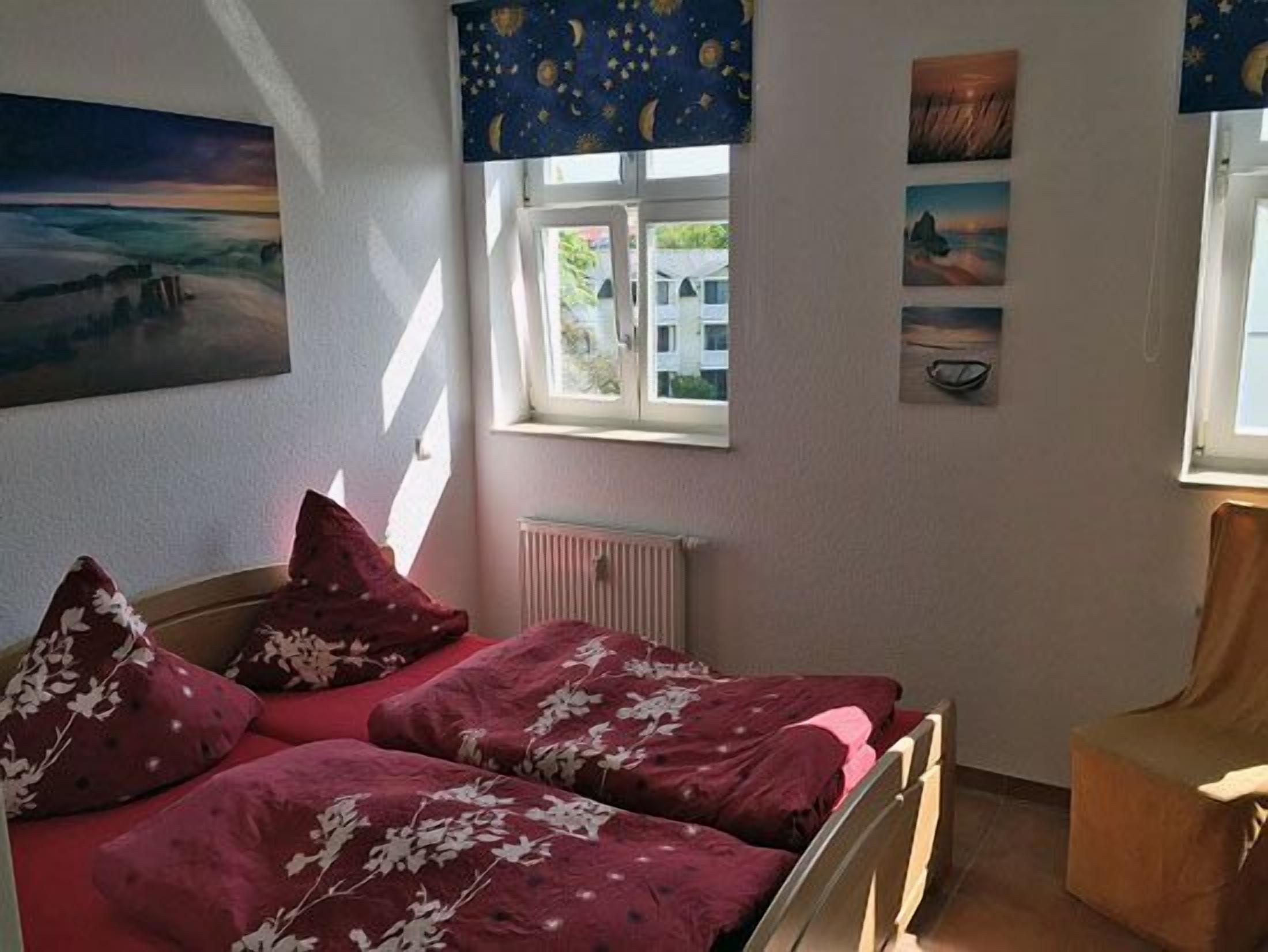 A bedroom with two beds, a radiator, and a window with curtains.