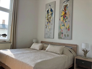 Ein Schlafzimmer mit einem Bett, zwei Wandgemälden, einem Nachttisch und einer Lampe.