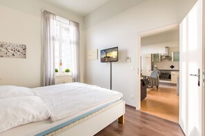 Ein Hotelzimmer mit einem Bett, einem Fernseher, einem Gemälde und Blick zur Küche.