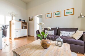 Ein modernes Wohnzimmer mit einer Couch, einem Couchtisch mit Vase und Blumen, einem Bücherregal und gerahmten Bildern an der Wand.