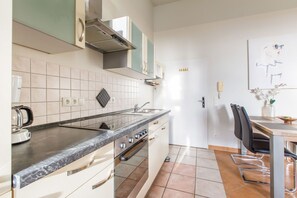Moderni keittiö, jossa on sisäänrakennettu uuni, kahvinkeitin sekä ruokailutila, jossa on tuoli ja pöytä.