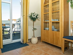 Quarto com porta de vidro deslizante que dá para uma área externa, armário de madeira com portas de vidro, cesta de vime com uma planta e uma mesa de jantar com cadeiras.