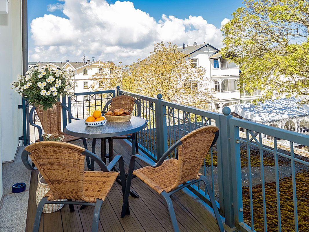A balcony with wicker chairs, a table with a fruit bowl, and a potted plant.