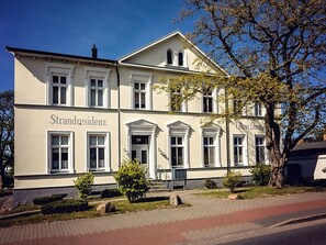 Ein Gebäude mit der Aufschrift 'Strandresidenz' an der Fassade, das ein symmetrisches Design mit zahlreichen Fenstern und einem zentralen Eingang aufweist.