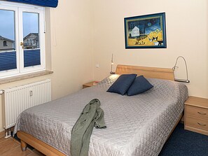 Ein Schlafzimmer mit einem Bett, einem Nachttisch, einer Nachttischlampe, einem Fenster mit Jalousien, einem Heizkörper und einem Bild an der Wand.