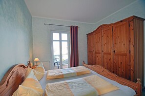 A room with two beds, a wooden wardrobe, a window with curtains, and a chair outside. - Just 100 meters from the sandy Baltic Sea beach, Wi-Fi, 1 bedroom, sleeps up to 4, with a balcony (Glowe)